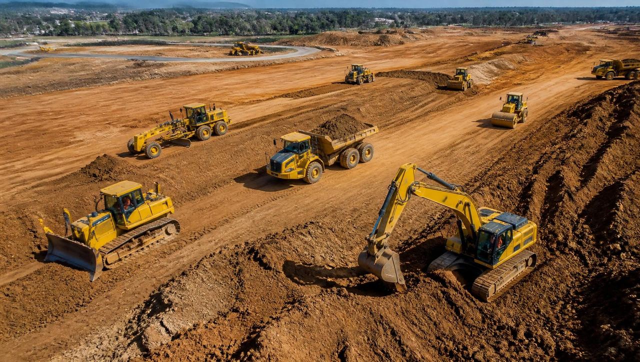 Aerial view of a large earthmoving site with yellow excavators, bulldozers, graders and rollers at work